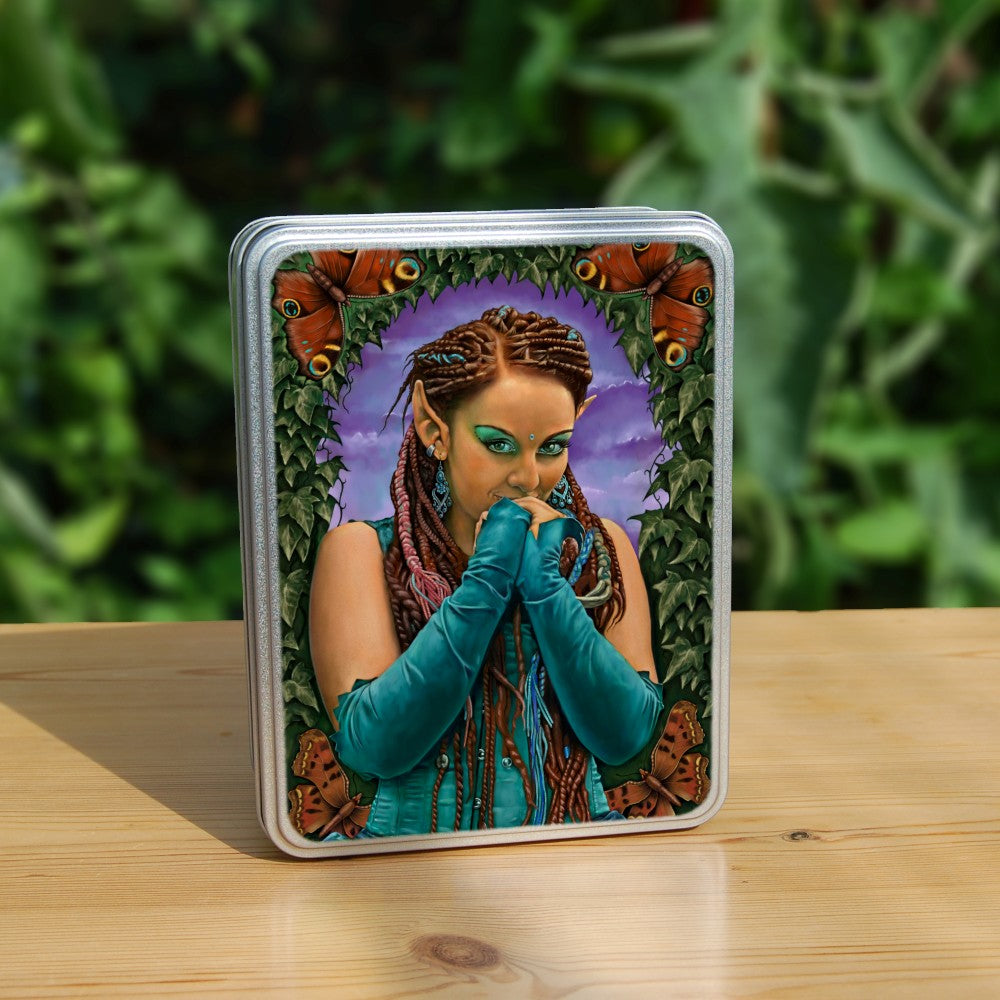 A brown-skinned female elf with long braided brown hair tied back, looks toward the viewer, hands held together in front of her mouth as though to suppress laughter. She wears a turquoise sleeveless dress and elbow-length arm sleeves. She's surrounded by ivy with a butterfly in each corner.