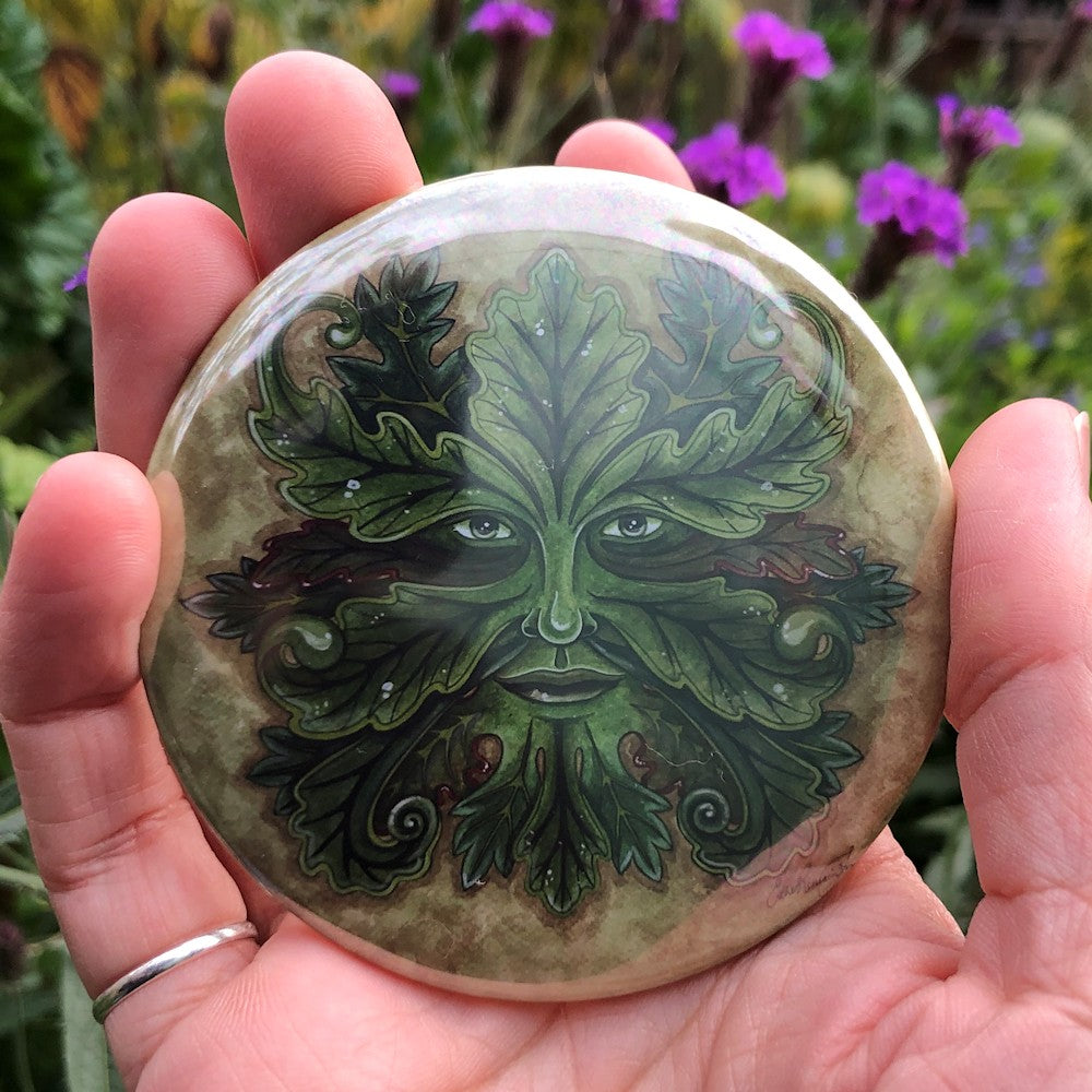 A Green Man. Green oak leaves grow out from around his eyes, nose and mouth. Some leaves have red edges. The background is a mottled pale green.