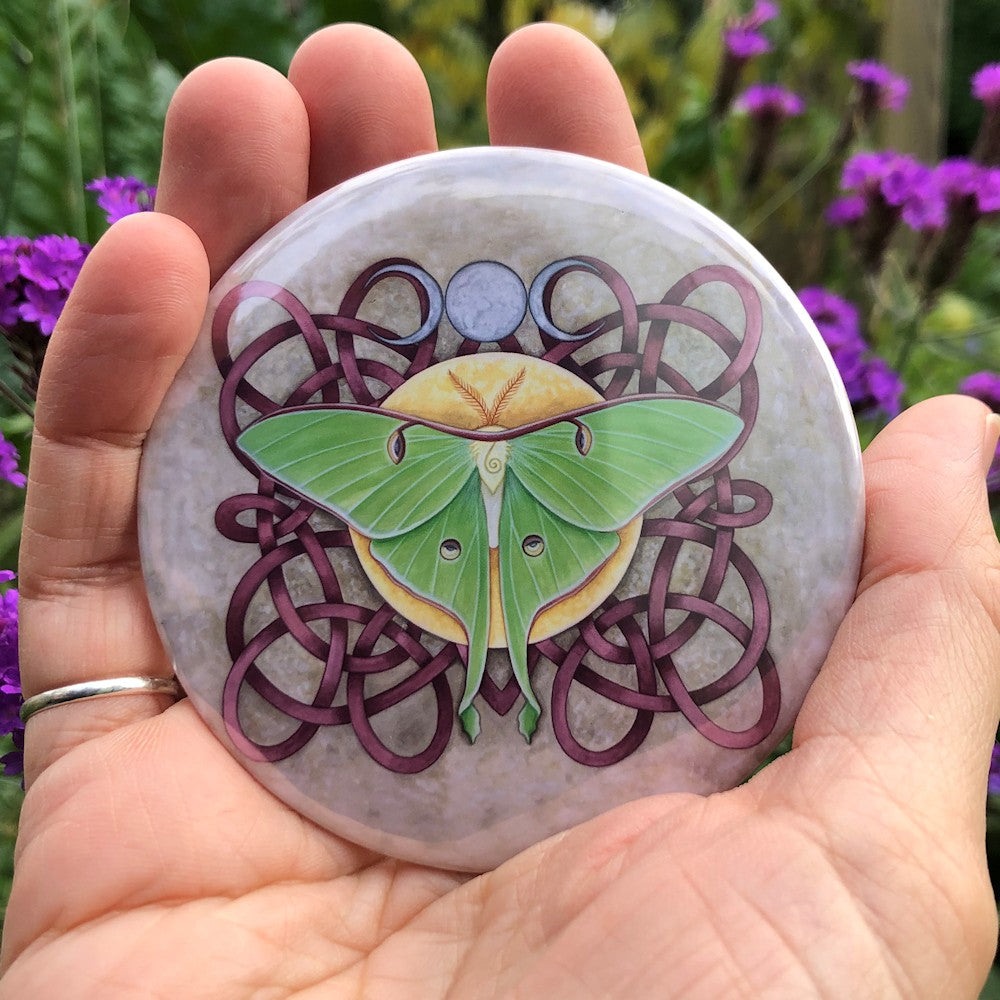 A deep pink Celtic-style knotwork fills the design. On top of the knotwork, in the centre, a Luna Moth sits on a yellow disc. There's a silver triple moon above.