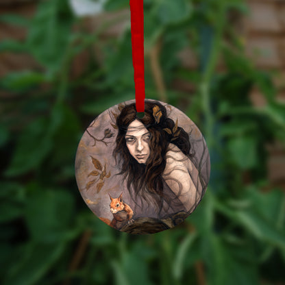 A circular hanging ornament with a red ribbon: The head and body of a young woman appears above a thick tree branch, upon which sits a red squirrel. The woman is turning her head as if to look behind her. She has long brown hair with leaves stuck in it. Autumnal leaves and branches fill the scene. Colours are reds, oranges and browns.