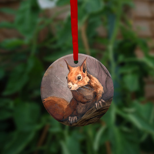 A circular hanging ornament with a red ribbon: A red squirrel sitting on a branch facing the viewer. Autumnal leaves and branches fill the scene. Colours are reds, oranges and browns.