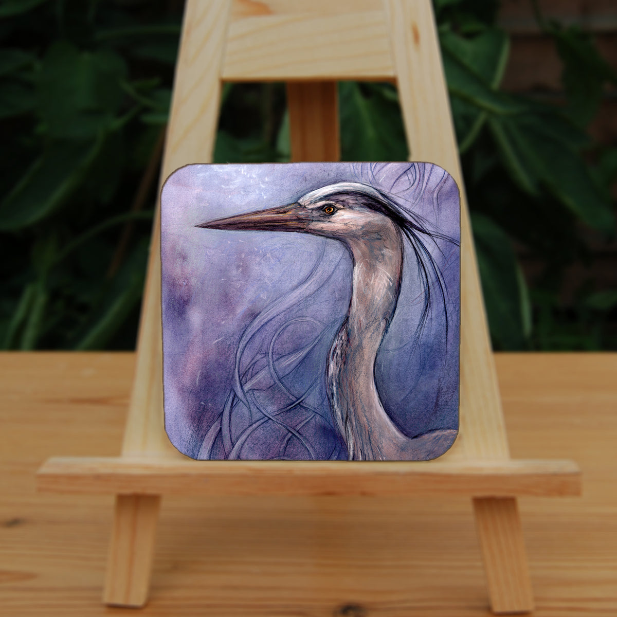 A square coaster: A sideways view of the head and neck of a heron. The background is a mottled purple with a swirl pattern.