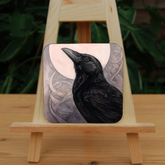 Square coaster: The head and body of a raven standing facing towards the left, head tilted upward, behind which is a full moon. The background consists of swirls in a pale pink-brown colour.