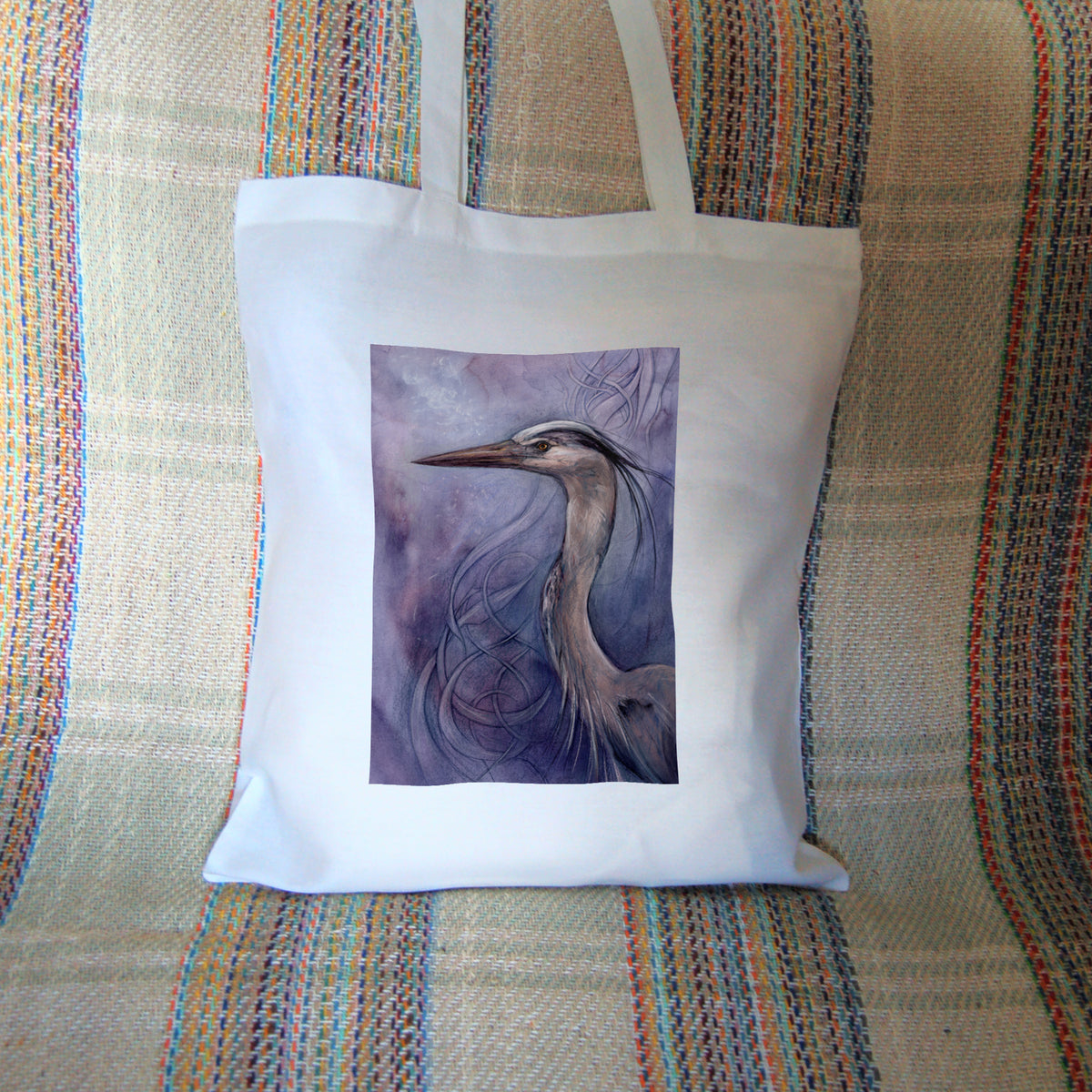 White tote bag: A sideways view of the head and neck of a heron. The background is a mottled purple with a swirl pattern.