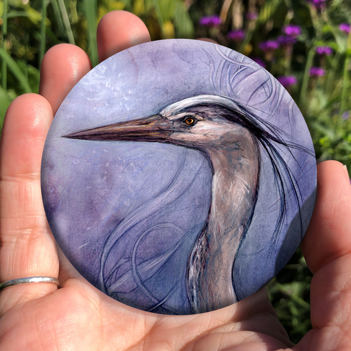 A hand holding a circular object: A sideways view of the head and neck of a heron. The background is a mottled purple with a swirl pattern.