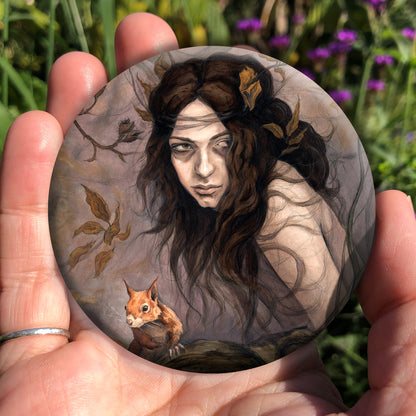 A handing holding a circular object: The head and body of a young woman appears above a thick tree branch, upon which sits a red squirrel. The woman is turning her head as if to look behind her. She has long brown hair with leaves stuck in it. Autumnal leaves and branches fill the scene. Colours are reds, oranges and browns.