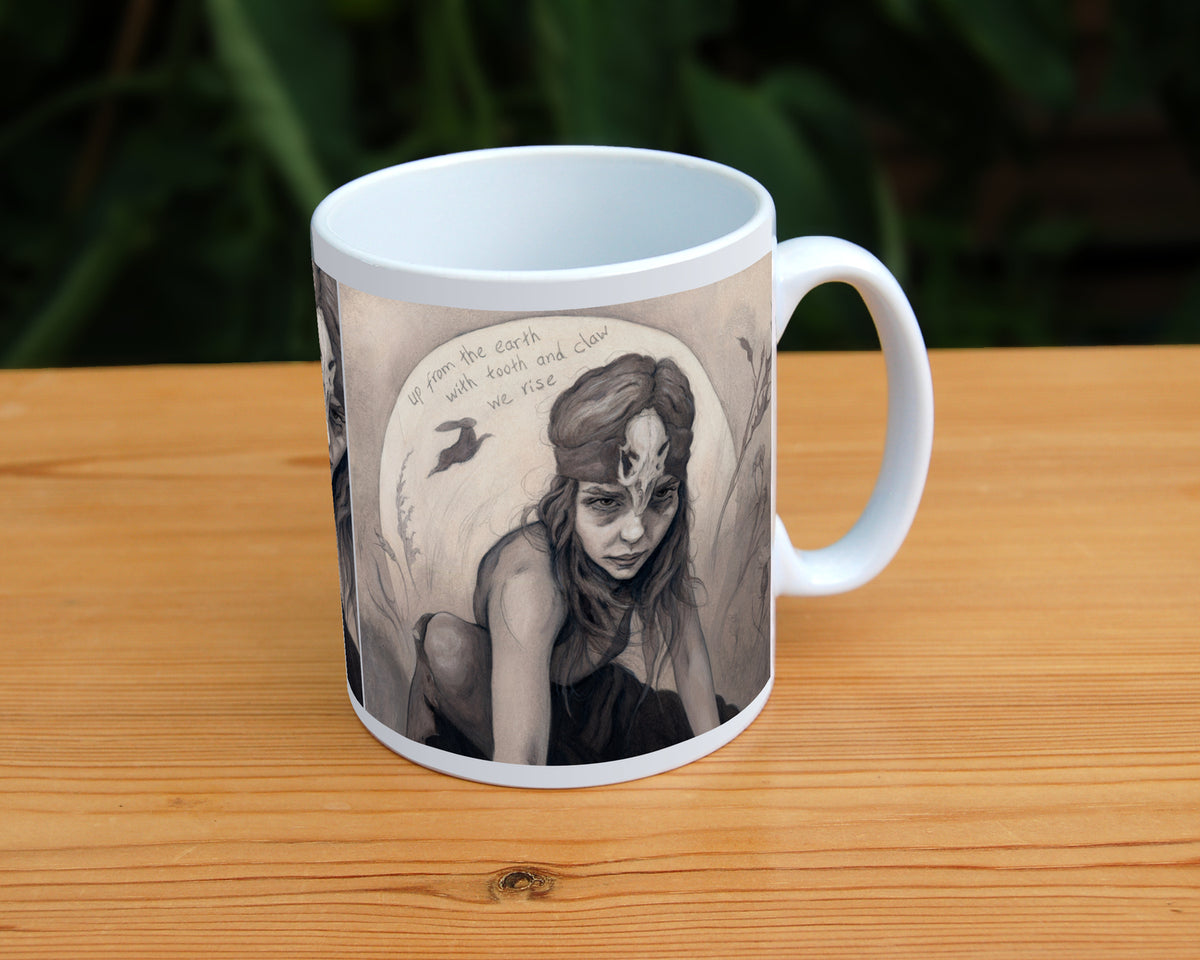 A white ceramic mug: A young woman crouches on a pile of stones, her hands resting on stones in front of her. The woman wears a headband with a raven skull attached to the front. A full moon rises behind her, and a silhouette of a hare leaps in front of it. An inscription over the moon reads: Up from the earth with tooth and claw we rise. Stems and flowers fill the rest of the scene.