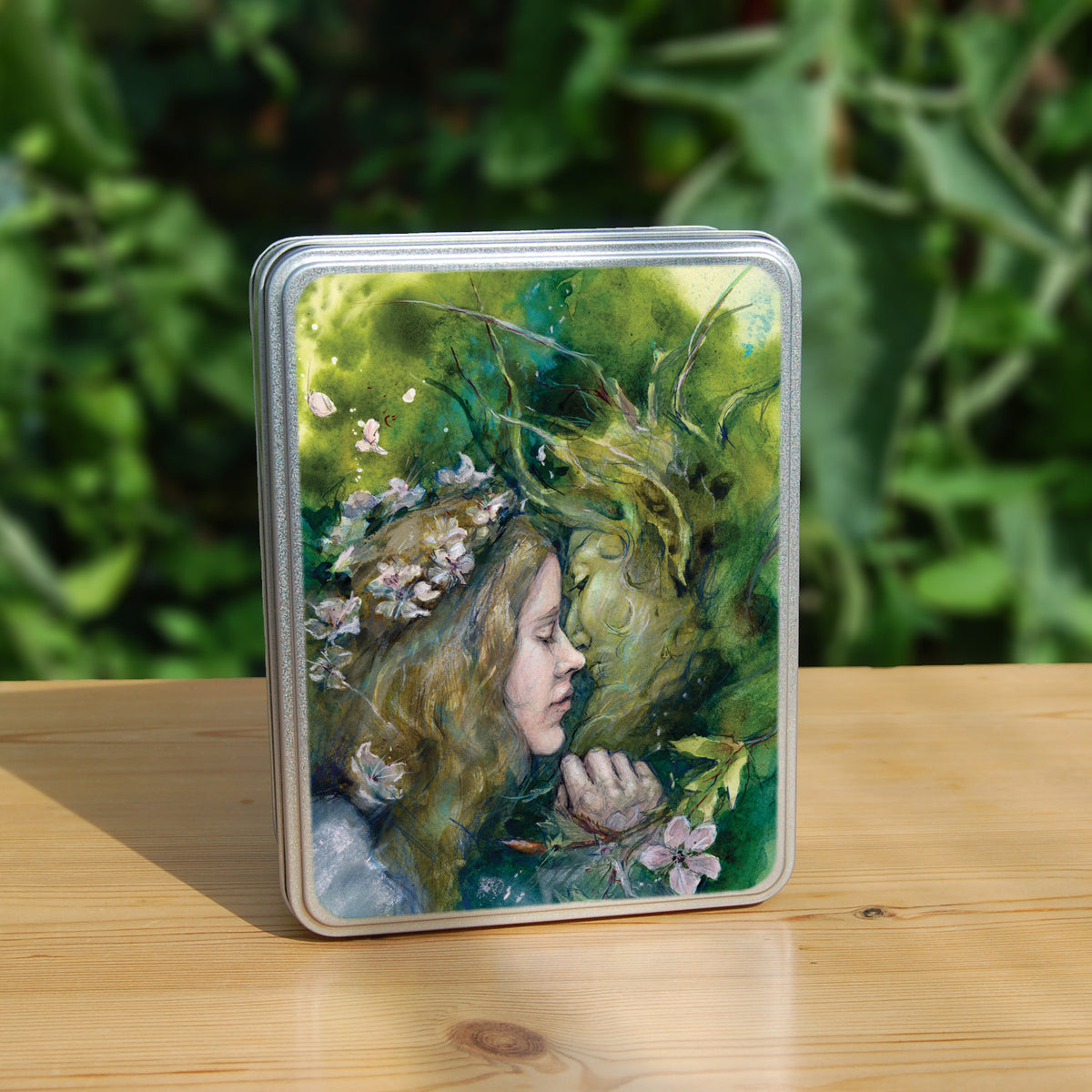 Rectangular metal tin: A young woman with a garland of pale flowers in her hair closes her eyes as she moves to kiss a green man.