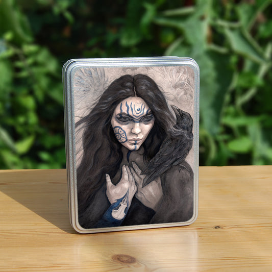 A rectangular tin: The head and shoulders of a woman with a raven sitting on her shoulder. She has long dark hair and her face is decorated with patterns in blue paint. Her hands are held together against her body. On her wrist she wears a blue band with a raven skull attached. The background is a mottled brown with feathers and swirls drawn within.