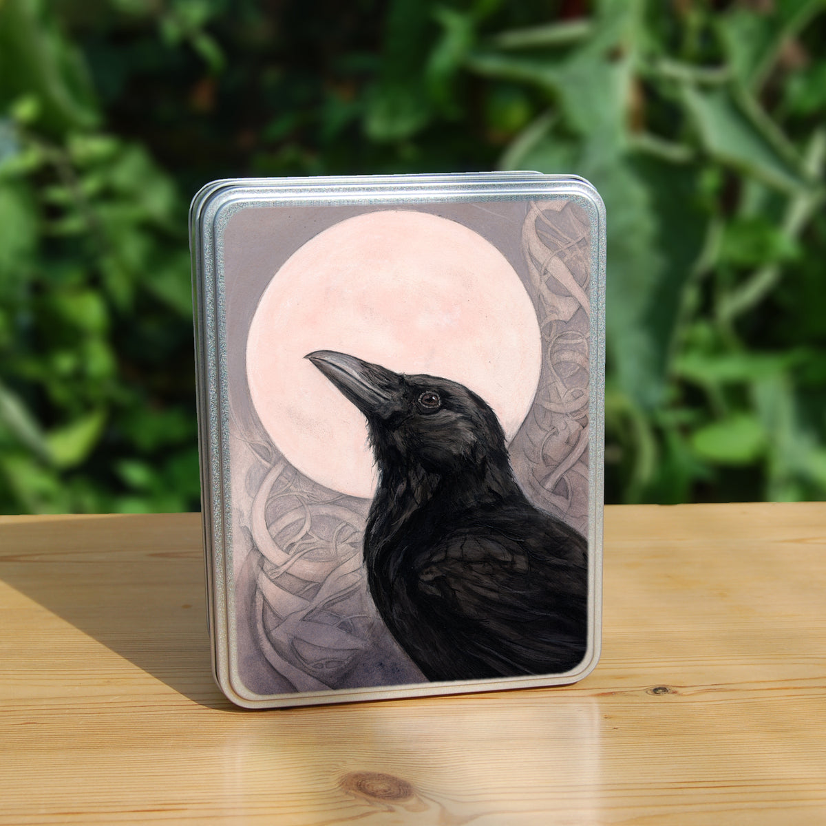 Rectangular tin: The head and body of a raven standing facing towards the left, head tilted upward, behind which is a full moon. The background consists of swirls in a pale pink-brown colour.
