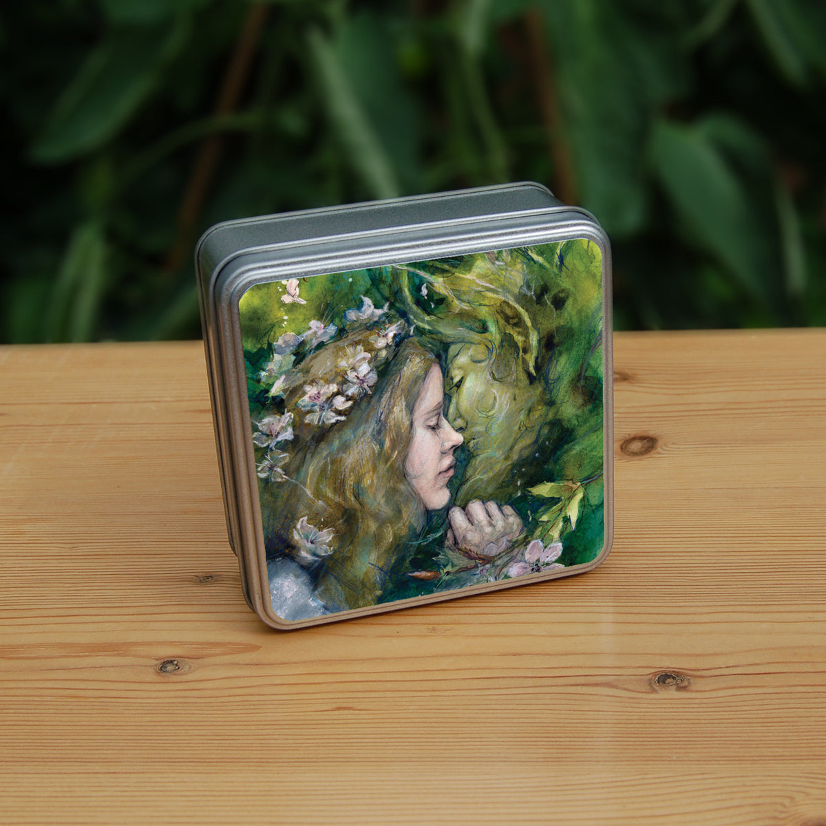 Square metal tin: A young woman with a garland of pale flowers in her hair closes her eyes as she moves to kiss a green man.