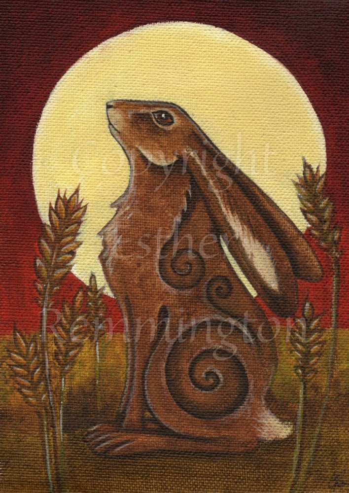 A large, reddish-brown hare dominates the design, sitting facing to the left, their head back and facing towards the sky, ears folded behind them. A large yellow moon fills the top two thirds of the design behind the hare. To the left and right are ears of wheat. The background is brown at the bottom and deep red around the moon.