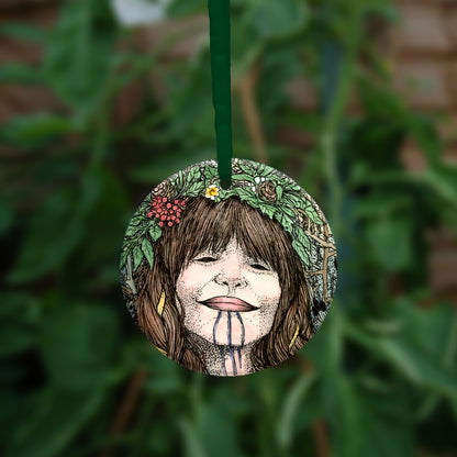 One side of the ornament. The head of a woman with long, plaited and bound brown hair, three drawn lines from her lip to her neck, and wearing a garland on her head. 