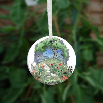 One side of the ornament. At the top there's a tree in full leaf, surrounded by clouds, but clearing to blue in the centre, and swifts wheeling all around. Beneath, the top half of the oval is a flower-filled meadow. A stag and badger stand either side, and a hare, blackbird, mouse, and other creatures are nestled within. The head and shoulders of a young woman lying on her back rise from the ground. 