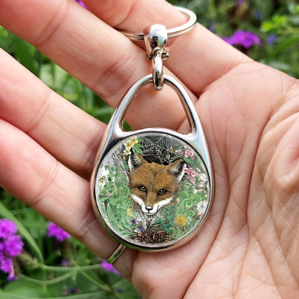 The head of a red fox looks towards the viewer. He's surrounded by a mass of leaves and flowers which rise out from a twisted tree trunk and tangled branches.