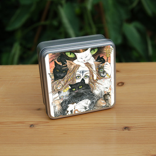 A mass of cats of all colours and in many poses surrounds the face of a red-haired woman with cat-slit eyes and ears, and a Eye of Horus symbol on her forehead. A white cat sits on her head. She holds a gold-coloured sistrum (a type of rattle) in one hand. The head of a much larger cat with green eyes appears above and behind them. Colours are oranges, reds, black and white.