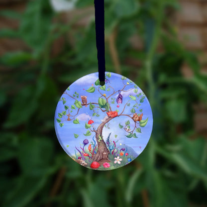 A tree with a curved trunk, curly branches and large green leaves, rises against a blue sky. Sitting on the branches are number of animals, including a fox, bat, spider, squirrel and owl. Also a tiny person holding an umbrella, and a very small cow! A fairy door can be seen at the foot of the tree, along with a hedgehog and colourful flowers and toadstools.