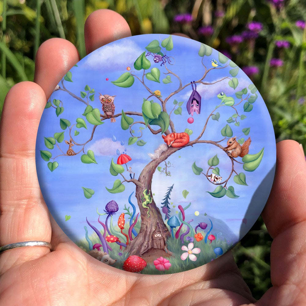 A tree with a curved trunk, curly branches and large green leaves, rises against a blue sky. Sitting on the branches are number of animals, including a fox, bat, spider, squirrel and owl. Also a tiny person holding an umbrella, and a very small cow! A fairy door can be seen at the foot of the tree, along with a hedgehog and colourful flowers and toadstools.