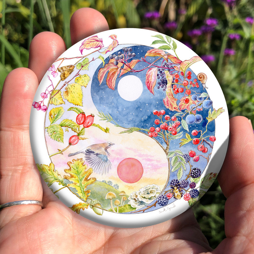 A Yin-Yang shape is surrounded by branches of native trees in autumn colours and some bearing fruit. The left hand half of the shape is filled with a pink/pale orange sky, and a large red sun forms the traditional 'dot' over a grassy hill. Autumn leaves and berries overlay the sky, a jay sings flies over, and fungi sit at the bottom. A moth sits on the outside curve. The right hand half features a dark blue sky with stars, with a white moon forming the 'dot'. Autumn leaves and berries overlay the scene.
