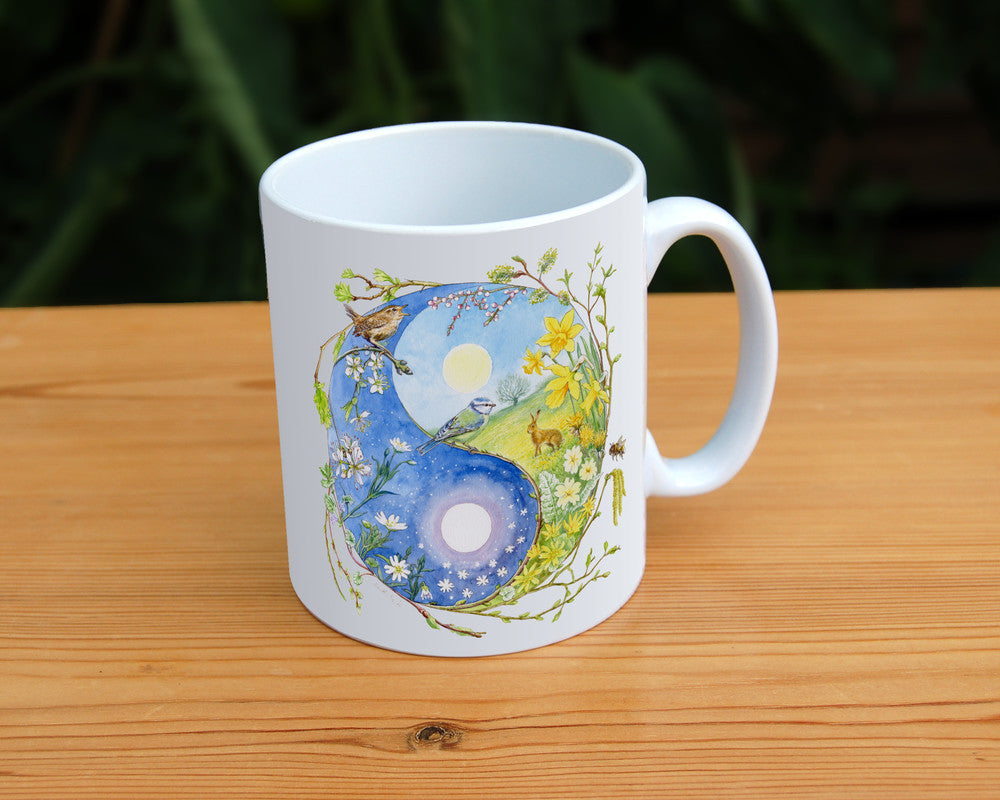 A Yin-Yang shape is surrounded by sprouting branches of native trees. The left hand half of the shape is filled with blue sky, and a large, watery sun forms the traditional 'dot'. White blossom and spring flowers overlay the sky, and a wren sings from a branch at the top. The right hand half features a hare sitting in a grassy field in a sunny day. A pale yellow sun forms the 'dot'. Yellow flowers overlay the scene. A blue tit sits on a branch forming the curve between the two sections.