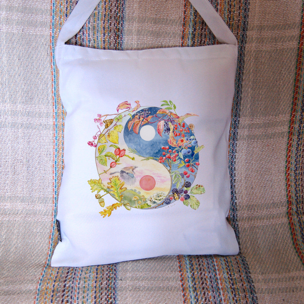 A Yin-Yang shape is surrounded by branches of native trees in autumn colours and some bearing fruit. The left hand half of the shape is filled with a pink/pale orange sky, and a large red sun forms the traditional 'dot' over a grassy hill. Autumn leaves and berries overlay the sky, a jay sings flies over, and fungi sit at the bottom. A moth sits on the outside curve. The right hand half features a dark blue sky with stars, with a white moon forming the 'dot'. Autumn leaves and berries overlay the scene.