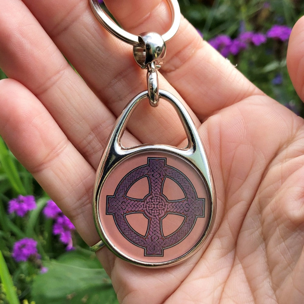 A Celtic cross design. Traditional Celtic knotwork runs through the inside of the cross and the outer ring, coloured red/purple. The background is a subtle orange.