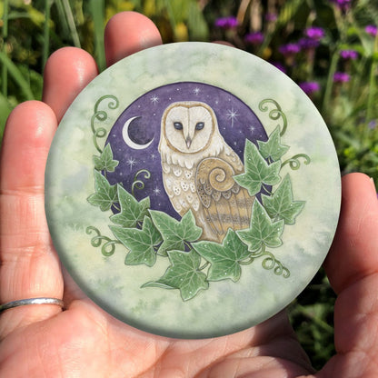 Illustration of the head and body of a brown and cream owl, enclosed in a circle with ivy leaves around the bottom two thirds, and a purple night sky with crescent moon and stars in the background. The bird is facing to the left, with its head turned to face the viewer. Stars can be seen in its eyes. The overall background is a mottled green.