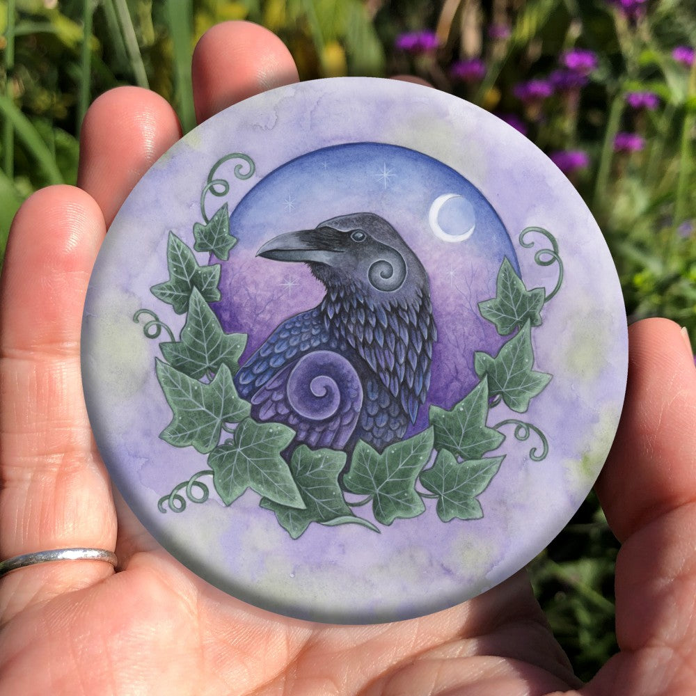 Illustration of the head and body of a raven, enclosed in a circle with ivy leaves around the bottom two thirds, and a night sky with crescent moon and stars in the background. The bird is facing to the right, with its head turned to the left. Swirls appear in the feathers on its neck and the top of the wing. The overall background is a mottled purple.